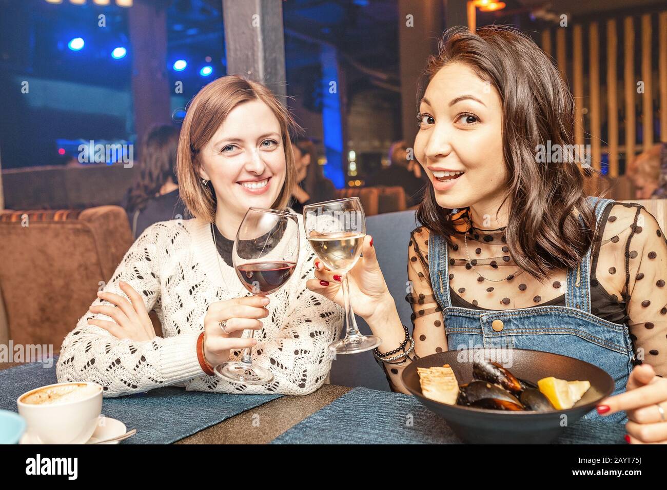 Two girl friends have fun and chat while drinking a glass of wine in a restaurant in a nightclub. The concept of relaxing and frienship Stock Photo