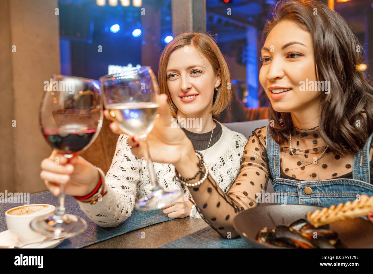 Two girl friends have fun and chat while drinking a glass of wine in a ...