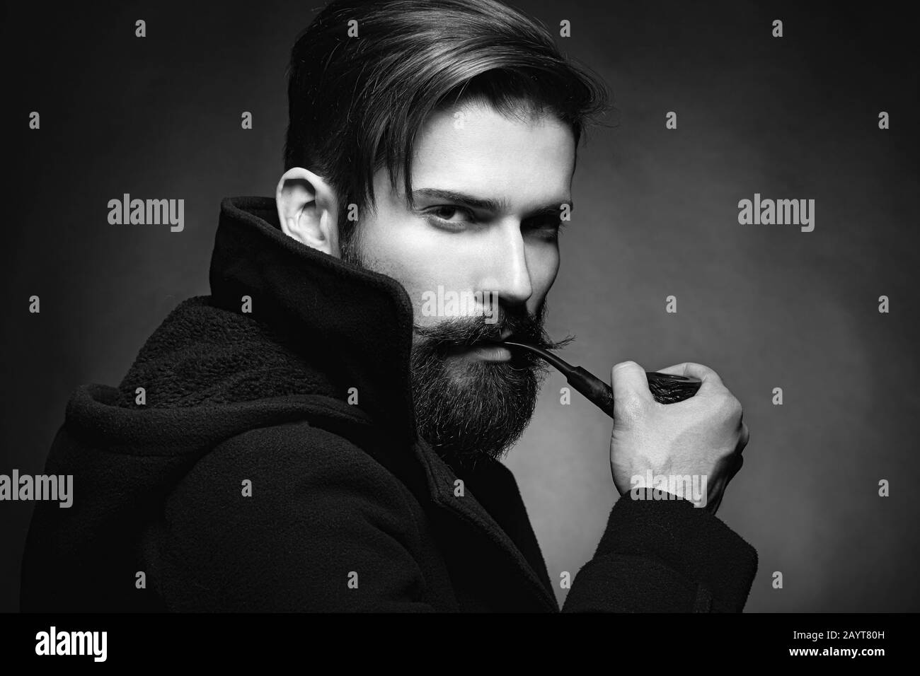 Brutal man with a beard and mustache Smoking a pipe. Close-up image of serious bearded man on dark background. Black and white photography Stock Photo