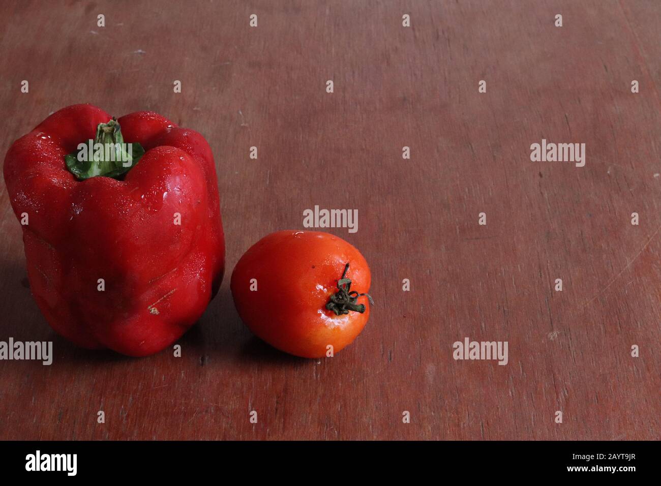 Red paprika and tomato against a wooden background to show concept of healthy diet, clean eating, vegan lifestyle and gastronomy Stock Photo