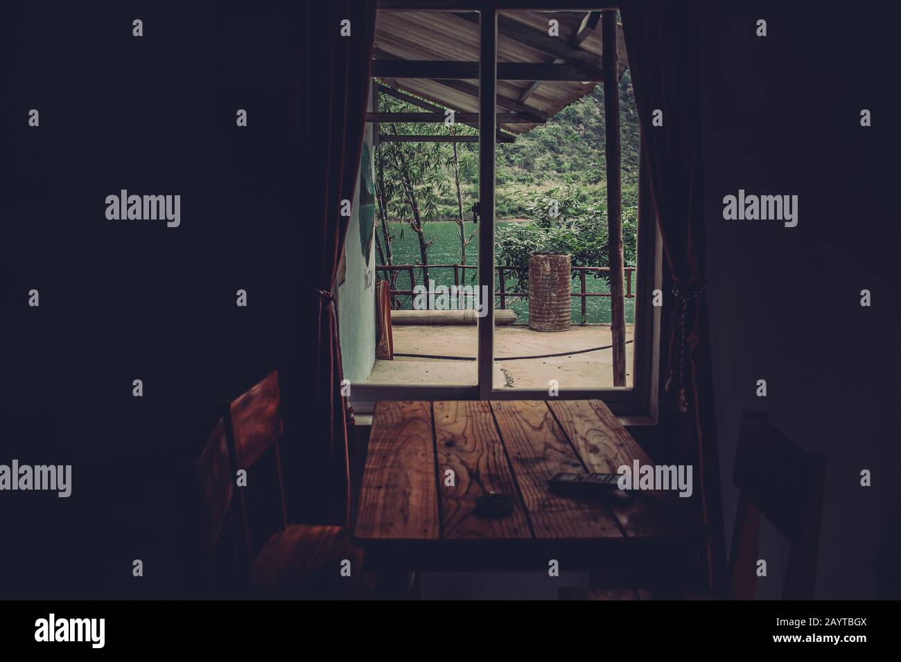 View of a river from inside the window of rustic wooden cabin in a dark and moody cinematic tone Stock Photo