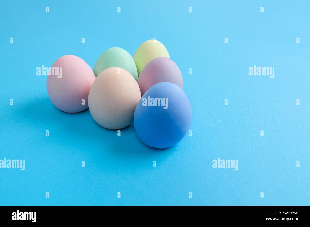 Easter Eggs painted in plain colors arranged in triangle shape on blue background with copy space Stock Photo