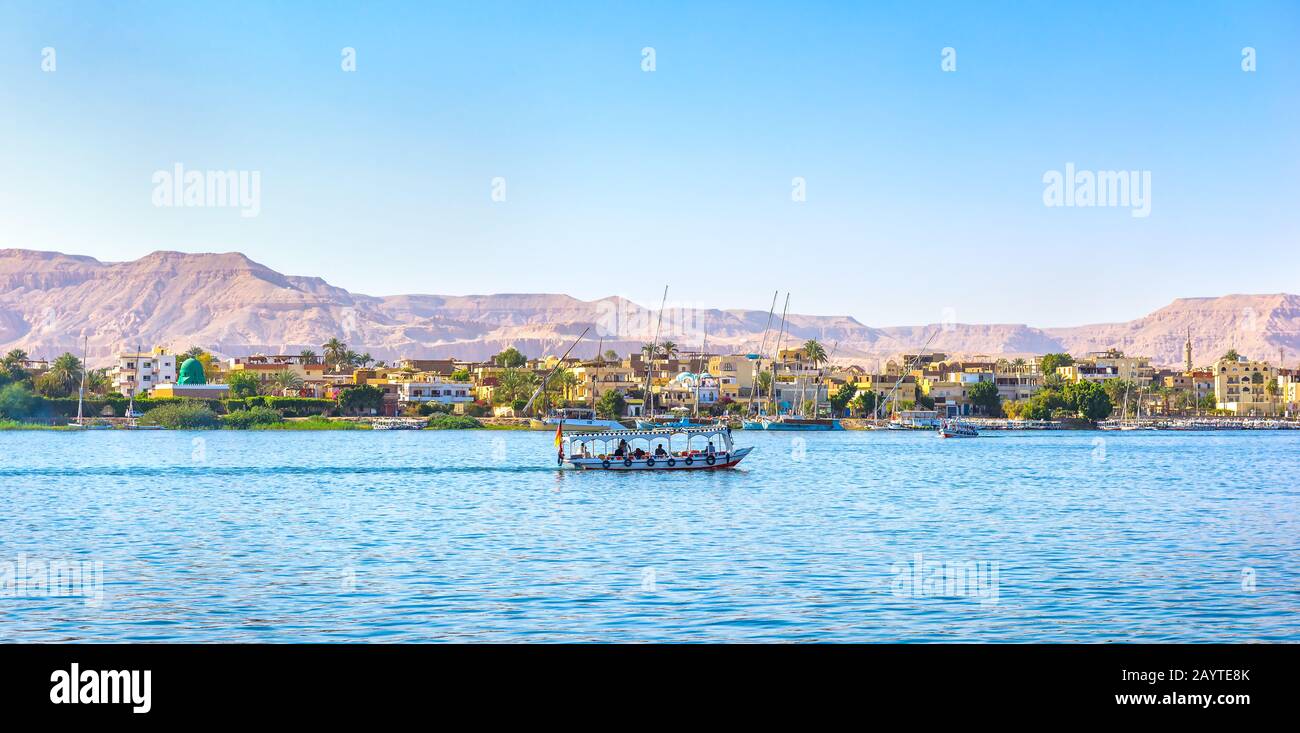 Touristic boat floating past the village on river Nile in Luxor, Egypt ...