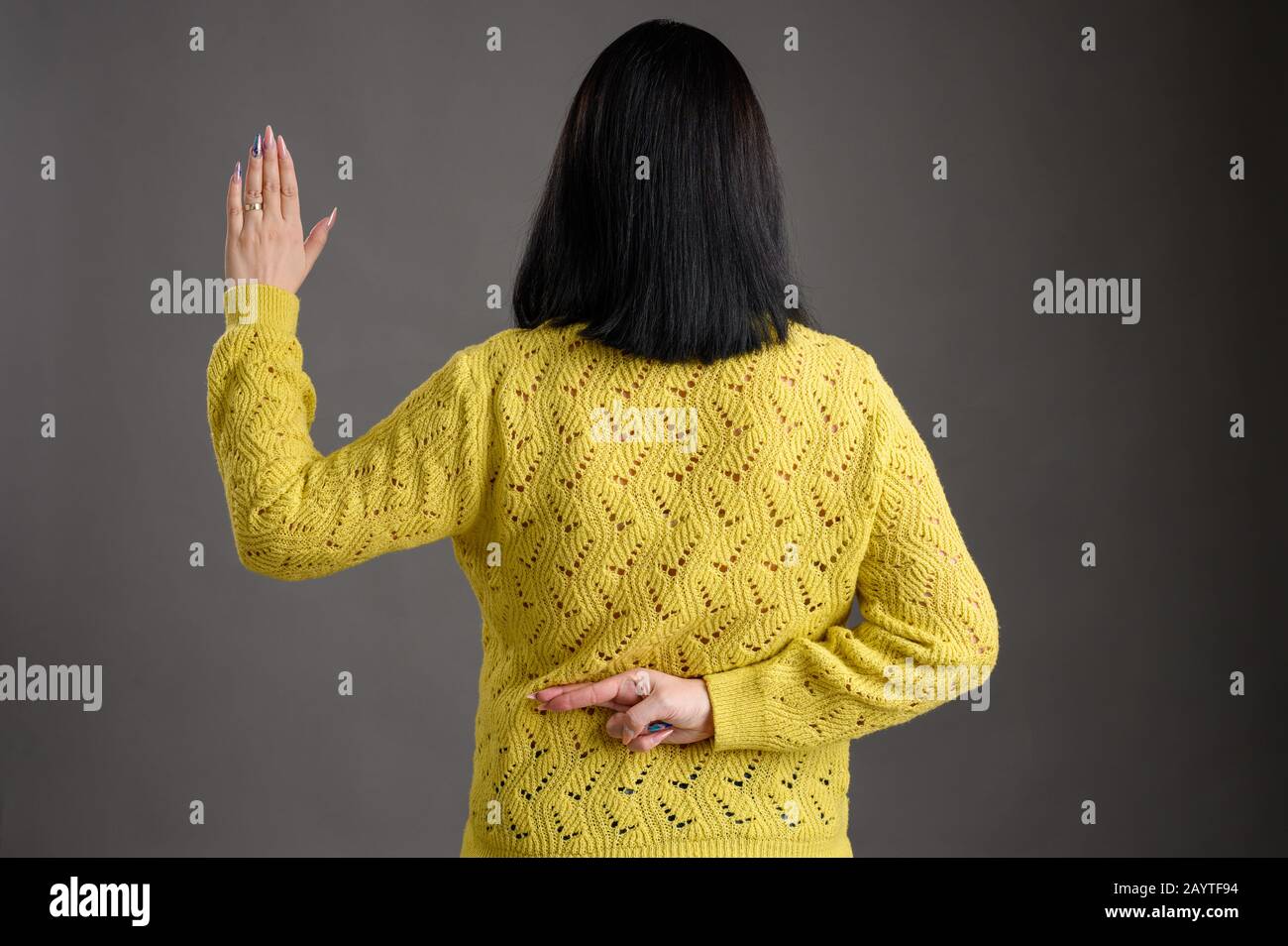 Young woman with black hair posing dressed in a yellow sweater showing fake oath isolated over grey background Stock Photo
