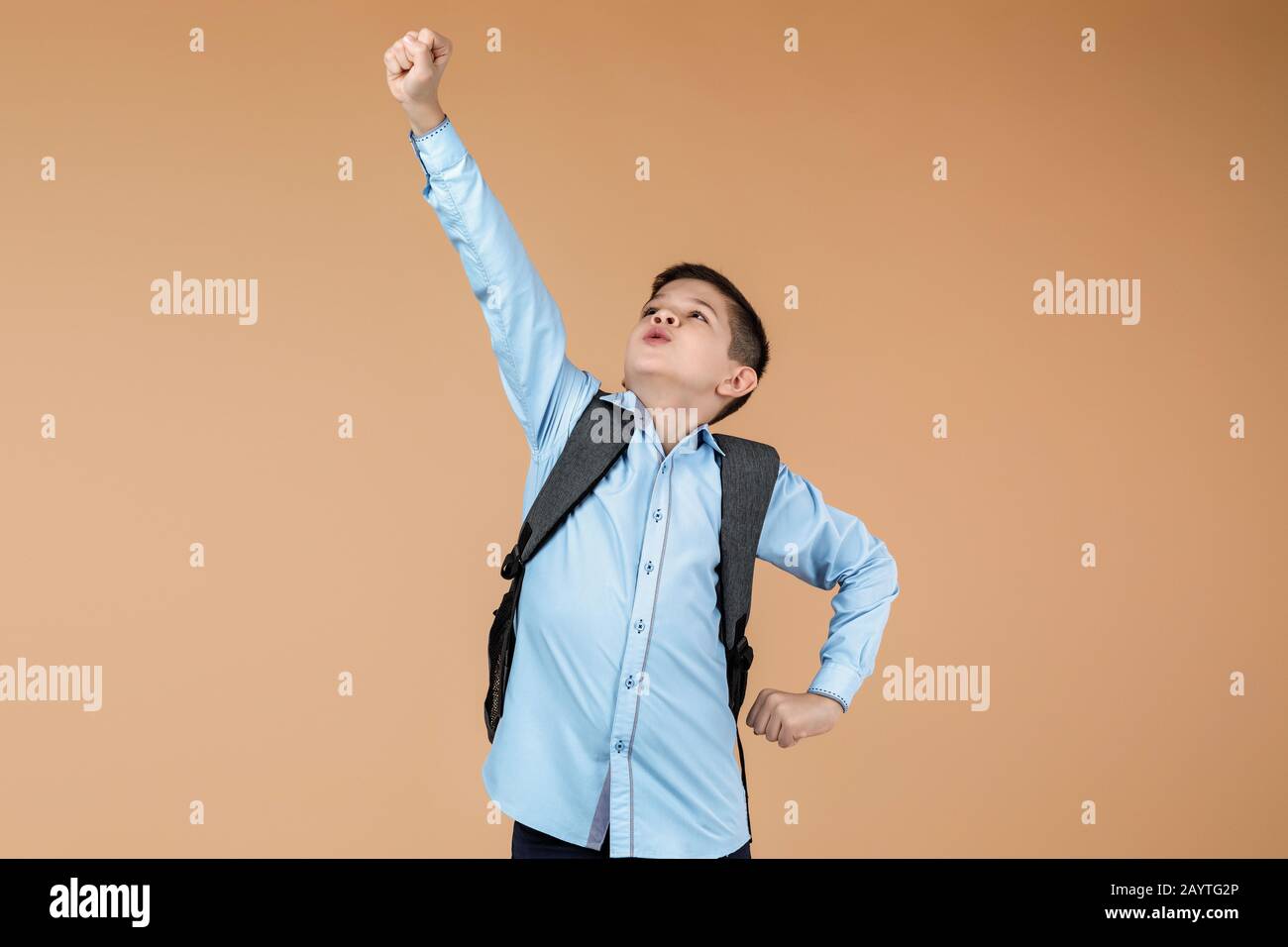 little cute school boy with backpack in superhero pose over yellow background. child ready to save the world. kid clenches his fist Stock Photo