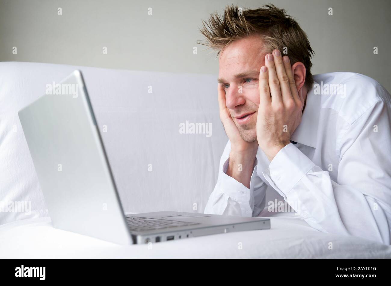Guy in white shirt kicking back on white sofa watching his computer ...