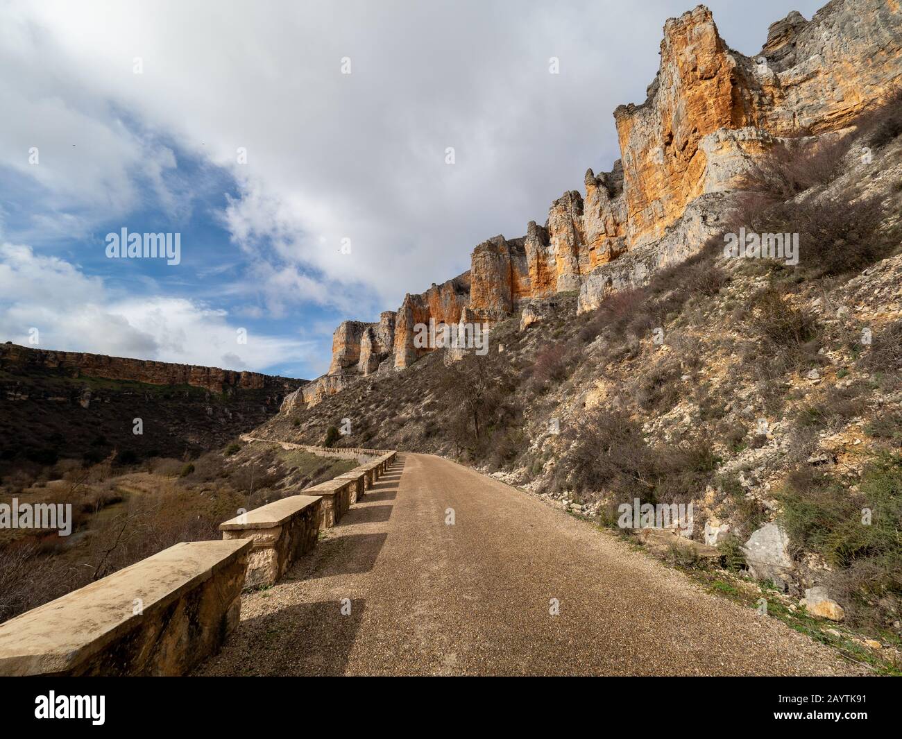 Sandy path in the middle of rocky mountains and a small stone wall with a stream on the side in Maderuelo in Spain Stock Photo