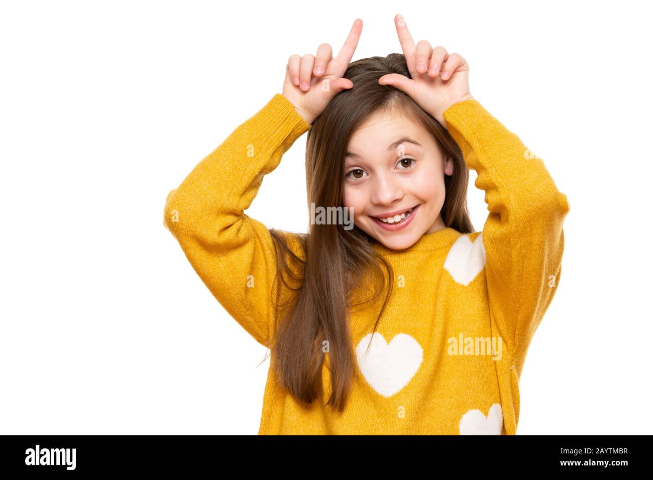 Studio shot of expressive cute child holding fingers behind head like bunny ears or horns, looking at camera and smiling. Lifestyle and beautiful peop Stock Photo