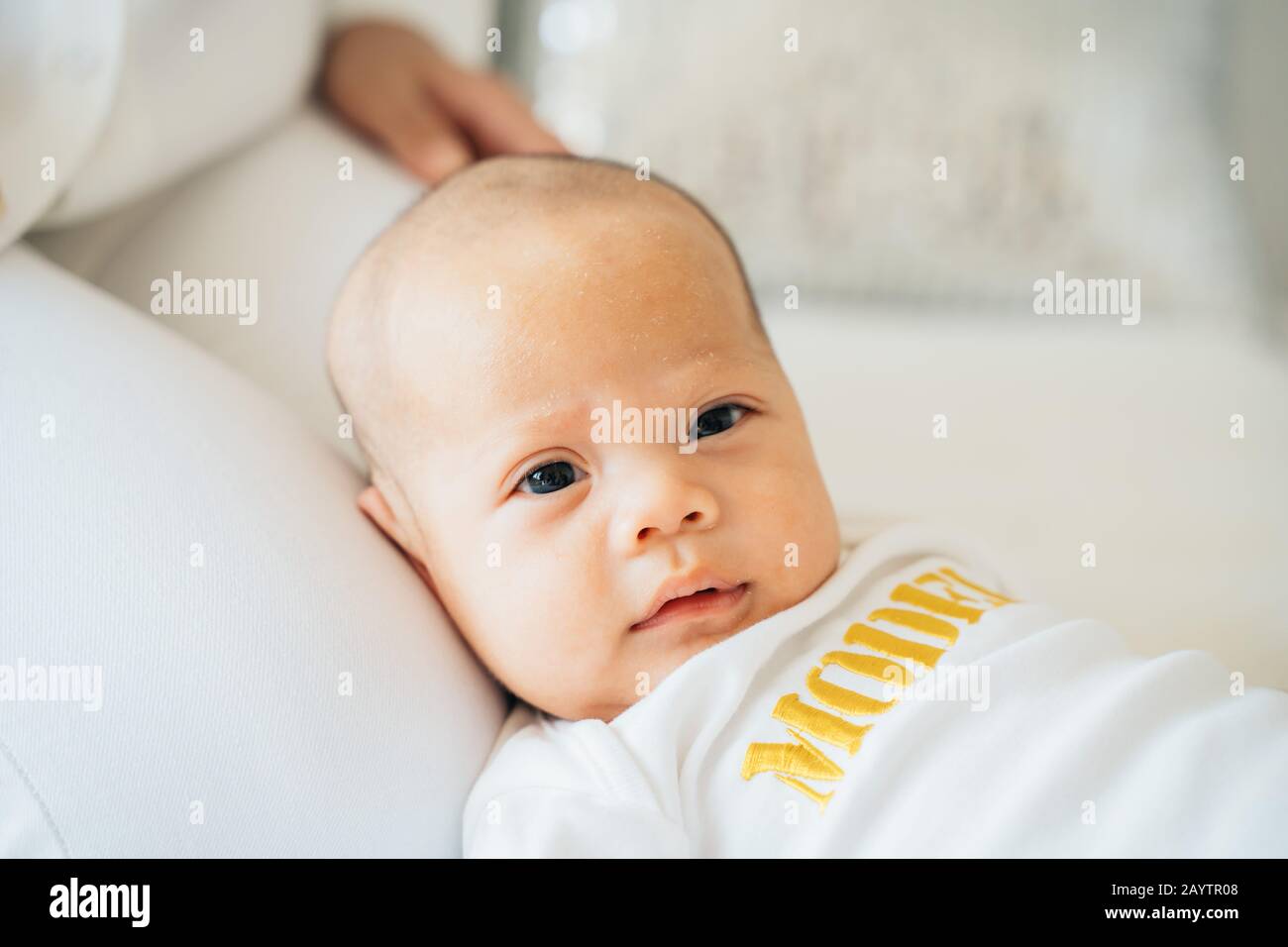 Closeup of calm adorable Asian toddler lying on lap of mother in bedroom of flat looking at camera Stock Photo
