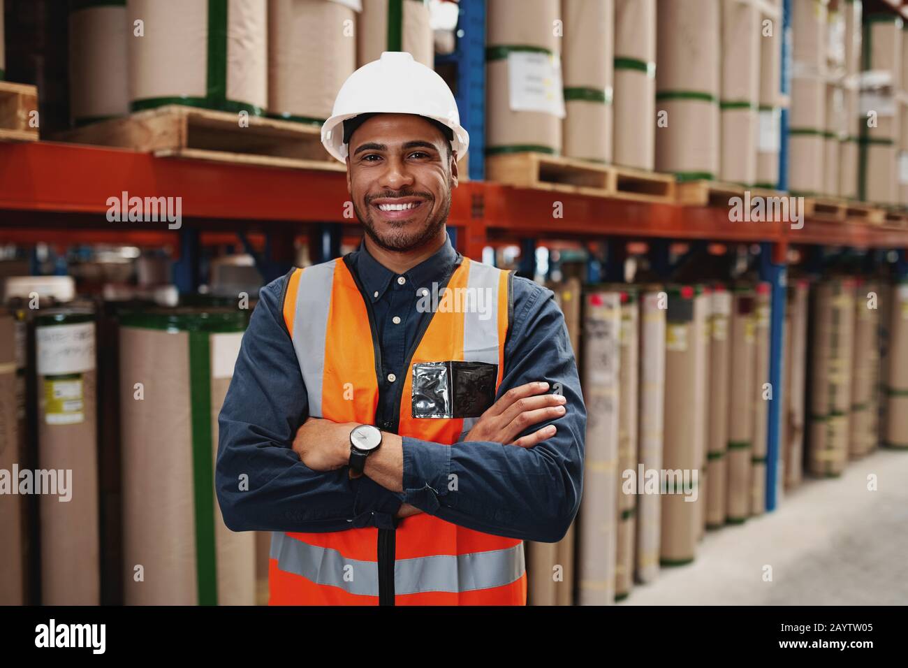 Confident african american man standing with folded arms in manufacturing unit with white helmet and uniform in factory Stock Photo