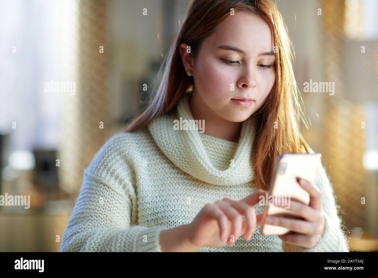modern young woman with red hair in white sweater with smartphone driving the growth of social media in the modern house in sunny winter day. Stock Photo