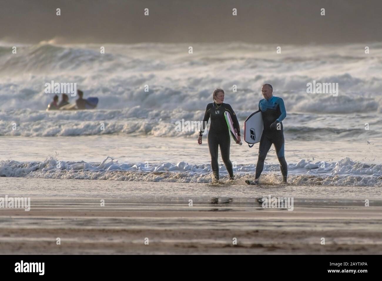 Mature bodyboarders carrying their bodyboards and walking out of the sea at Fistral in Newqay in Cornwall. Stock Photo