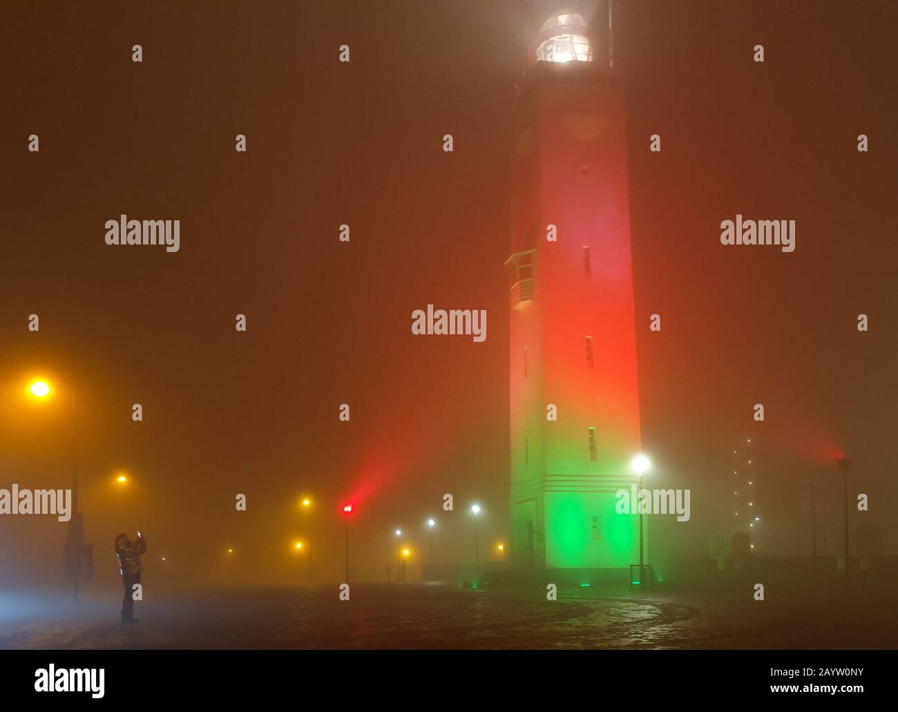 woman taking pictures of the illuminated lighthouse in the mist, Netherlands, Noordwijk aan Zee Stock Photo