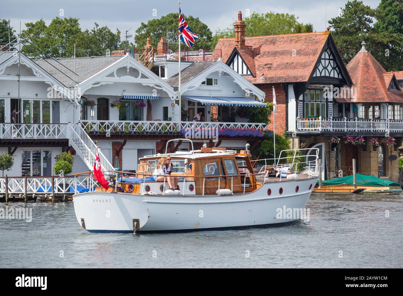 The classic 1965 cabin cruiser or Motor yacht 'Nodens' passes riverside houses on the Thames at Henley-on-Thames Stock Photo