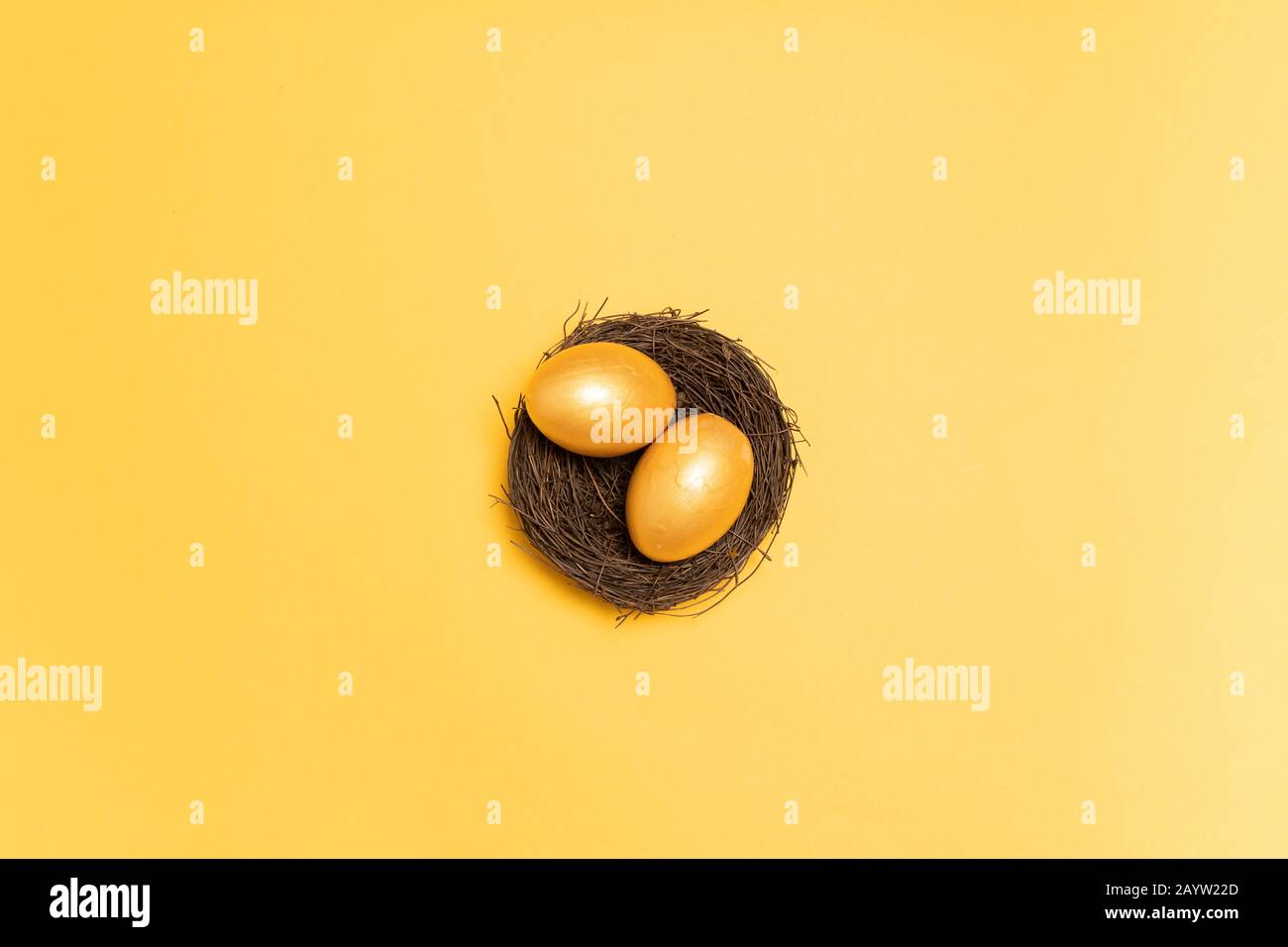 Top view of gold easter decor eggs in wicker nest on yellow background. Holiday composition card Stock Photo