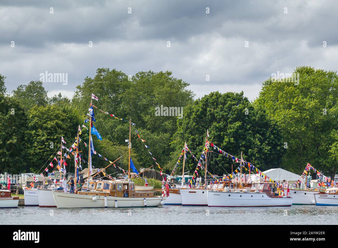 The classic Dunkirk Little Ships moored on the Thames near Henley-on-Thames at the Thames Traditional Boat Festival with bunting and flags and trees b Stock Photo