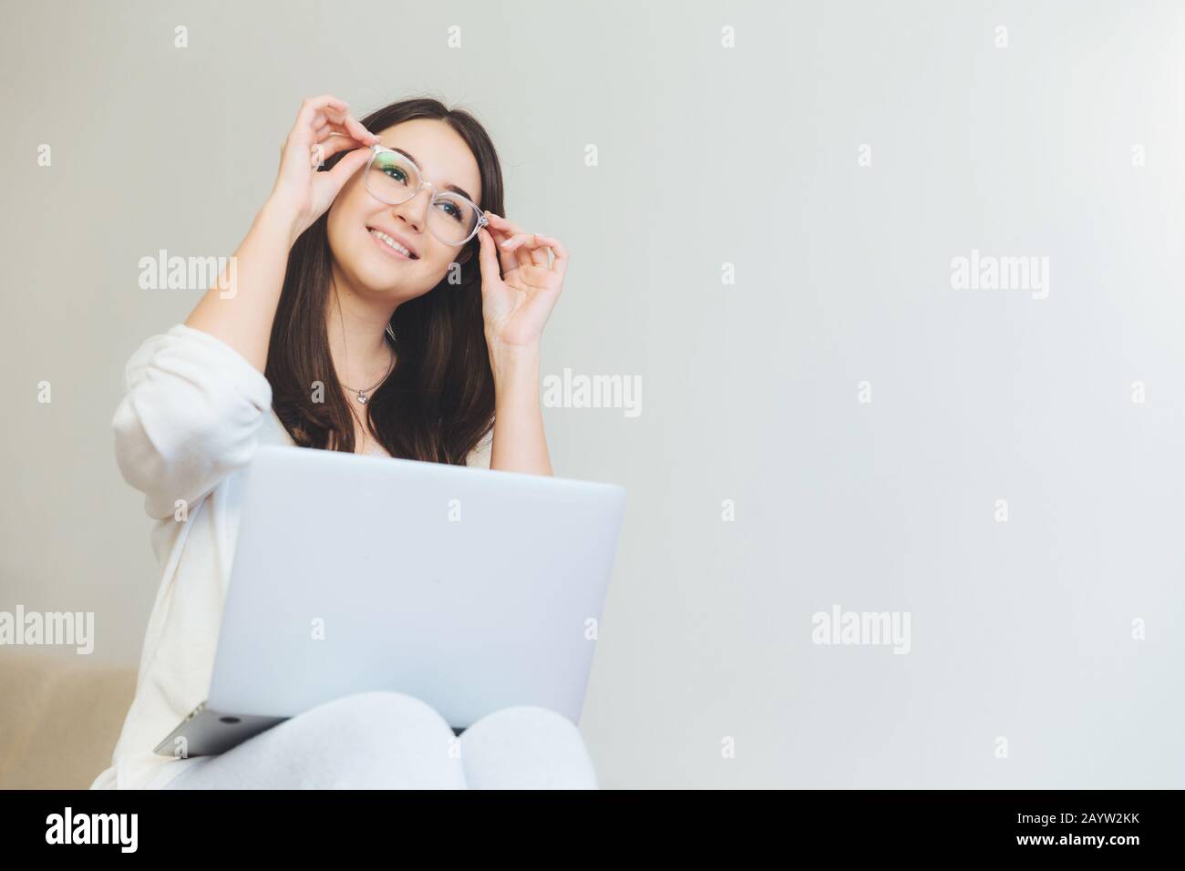 Positve female being glad to finish her course paper, works on laptop computer. Creative female web designer watches video with new graphic ideas, sit Stock Photo