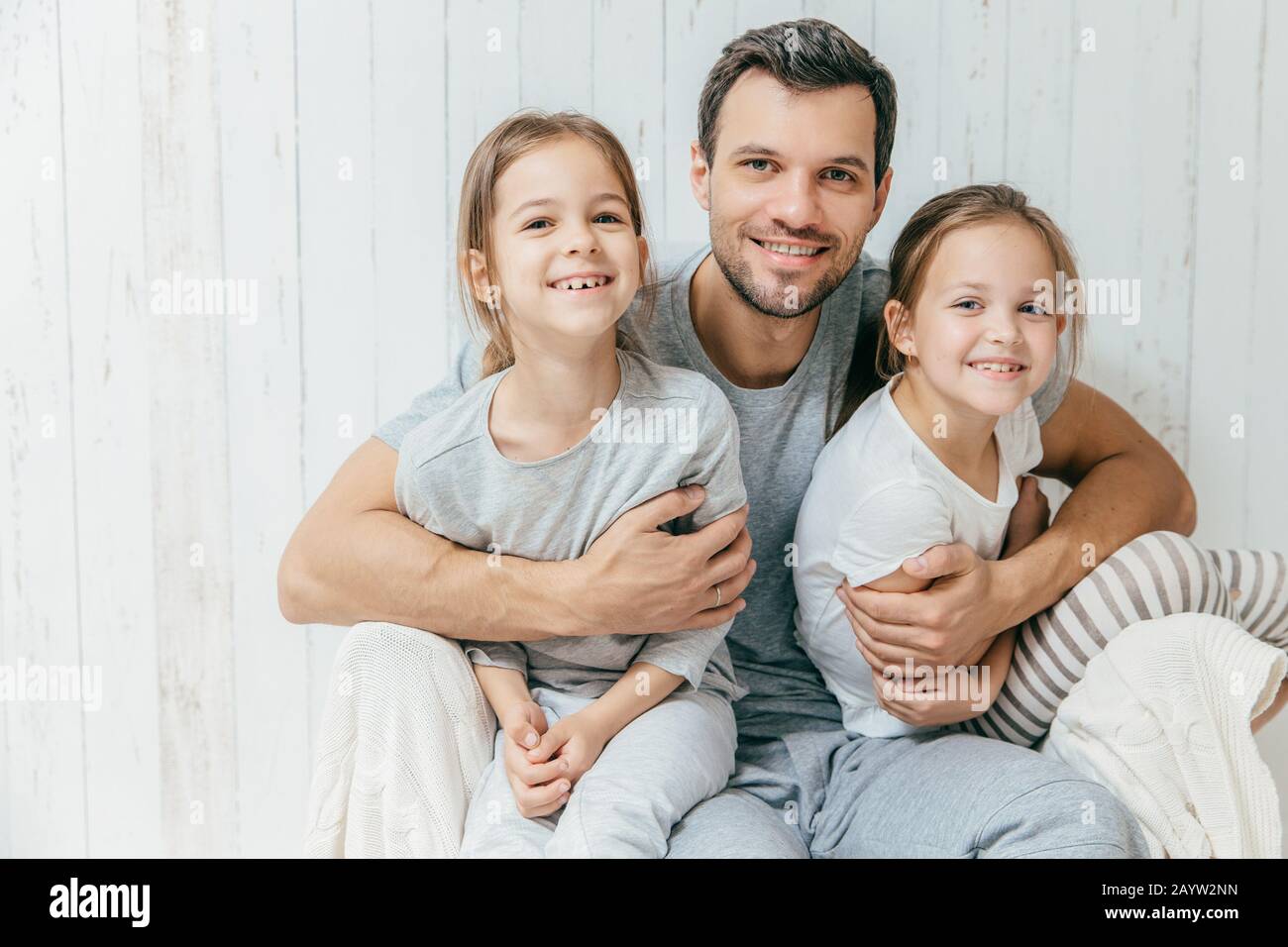 Portrait of happy young father embraces his two daughters, loves them very much, pose together