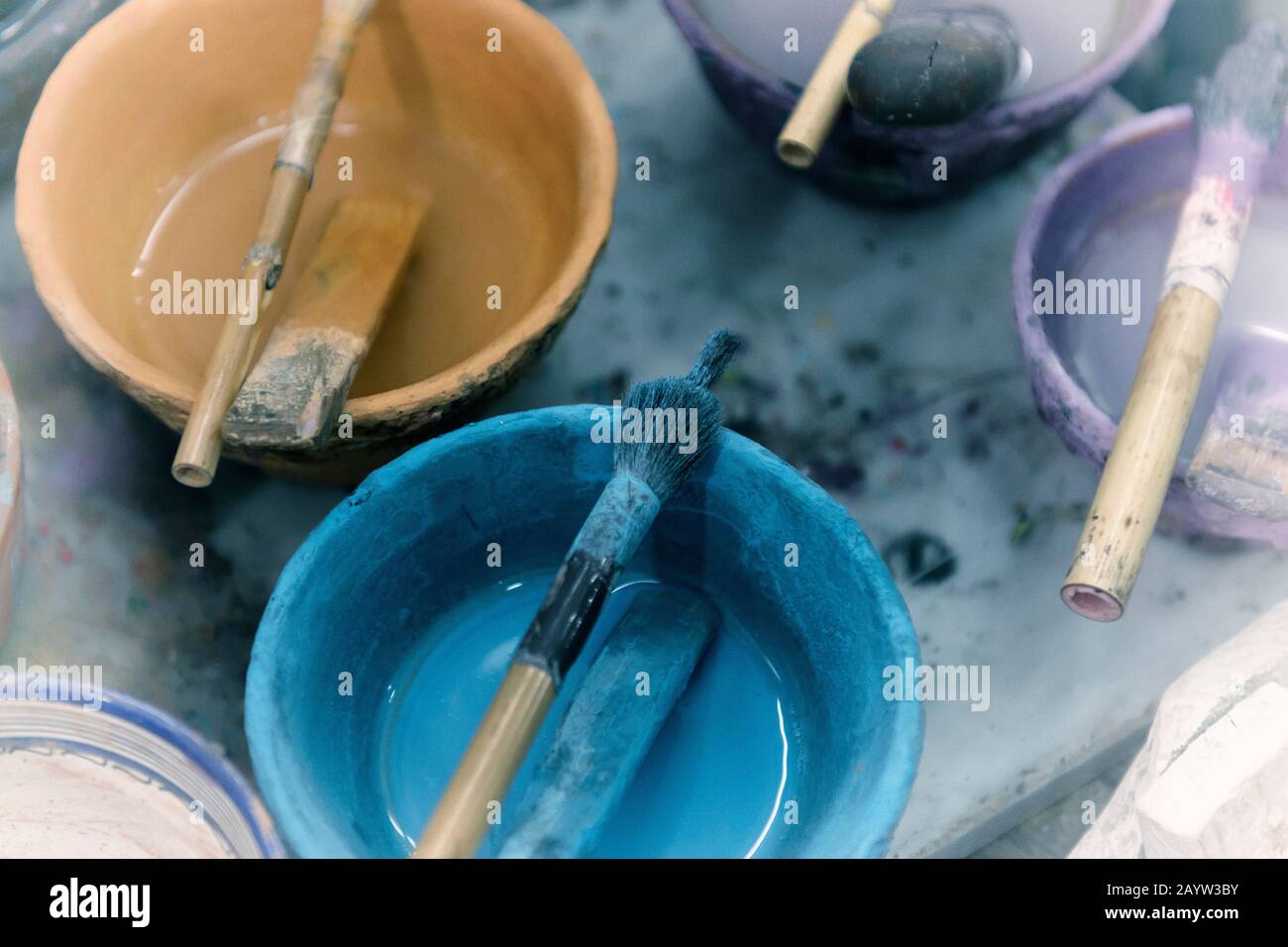 Paint in bowls with simple brushes in an artist studio. Vintage background image with film grain. Stock Photo