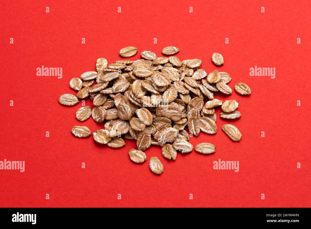 Pile of oat rye flakes on red color background Stock Photo