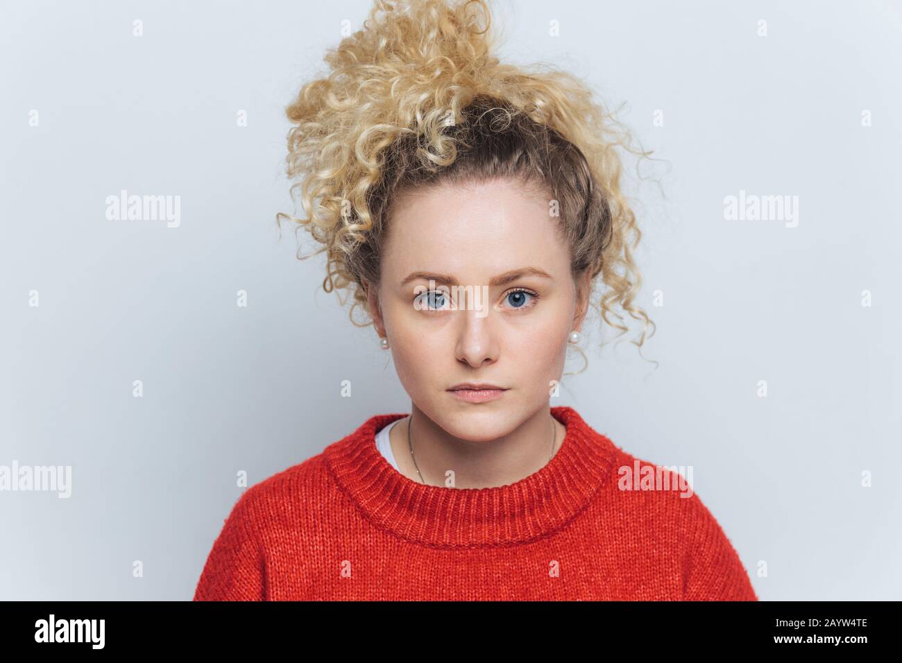 Headshot of serious pleased beautiful woman with healthy skin, blue eyes and curly hair, dressed casually, isolated over white studio background. Peop Stock Photo