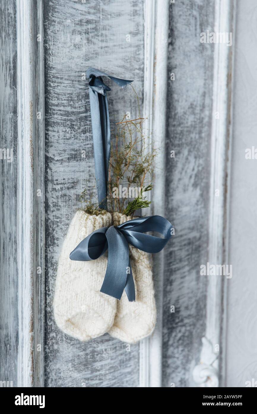 Photo of two knitted warm mittens hanging, decorated with twig of firtree and ribbon. Warm winter clothes. Pair of wool gloves against wooden ancient Stock Photo
