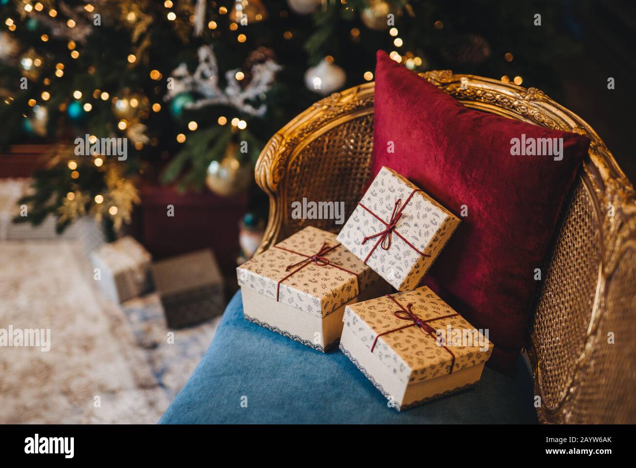 Three wrapped present boxes on armchair near Christmas fir tree. Design or idea for postcard. New Year composition with decorated fir tree and gifts. Stock Photo