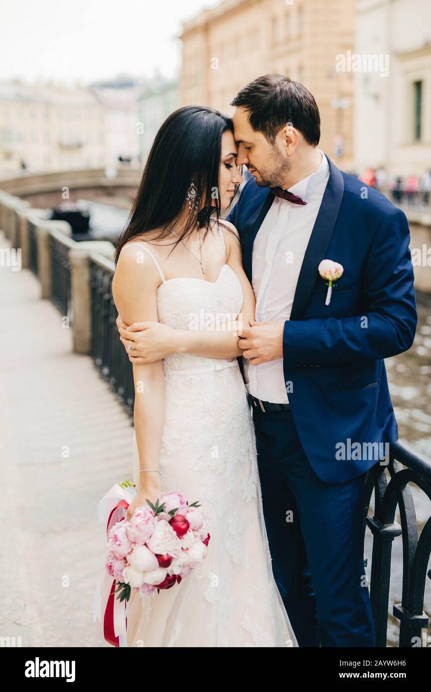 Romantic couple stands on bridge stand close to each other, look affectionately at each other, feel love and passion. Handsome bridegroom and bride in Stock Photo
