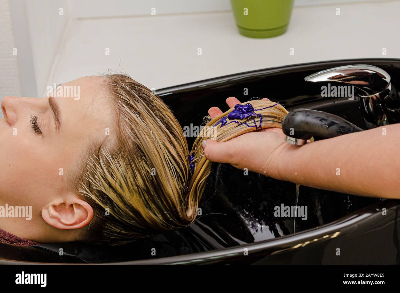 Hair stylist applying coloring purple shampoo after hair dyeing Stock