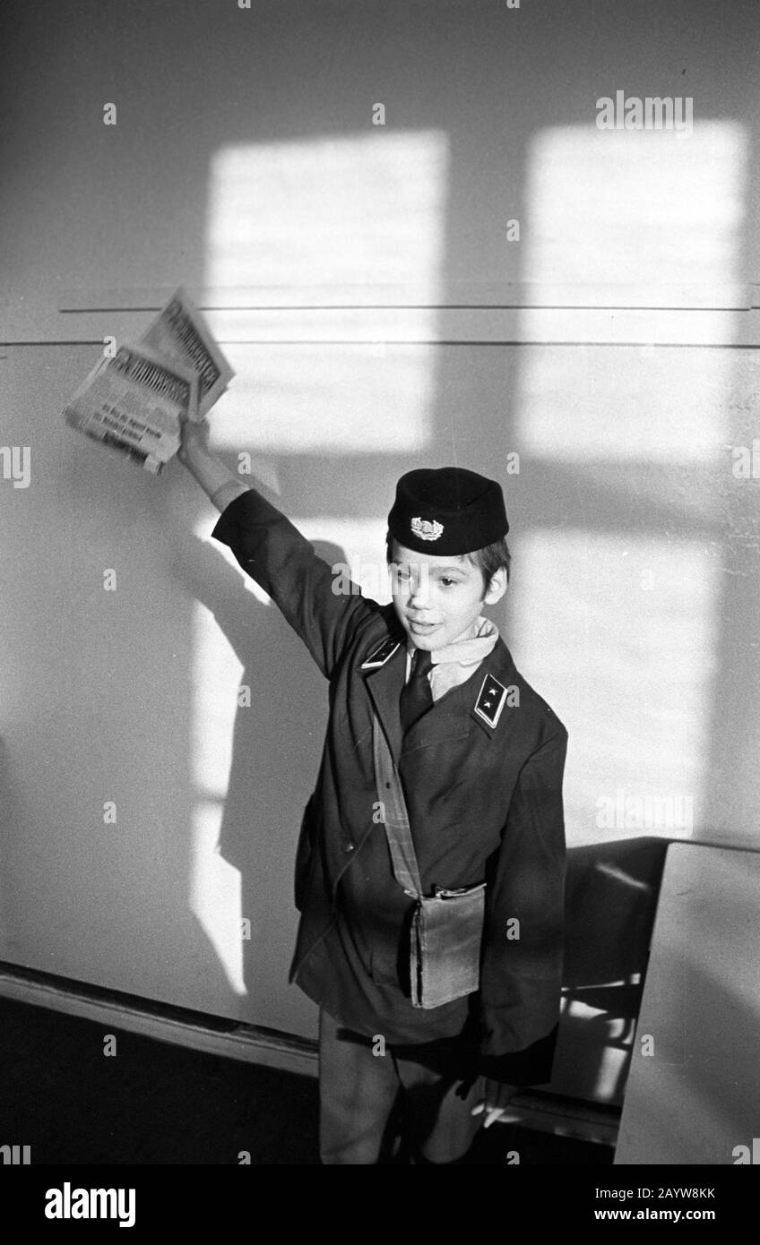 01 January 1979, Saxony, Leipzig: A child in a GDR postal uniform shows editions of the company newspaper 'Der Bauarbeiter' at the end of the seventies. Larger combines and state-owned enterprises published their own newspapers - usually monthly or fortnightly - as company newspapers. This is the newspaper of the SED's operating party organisation of the VEB BMK Süd (construction and assembly combine), a combined company of Industriebau Leipzig. Photo: Volkmar Heinz/dpa-Zentralbild/ZB Stock Photo