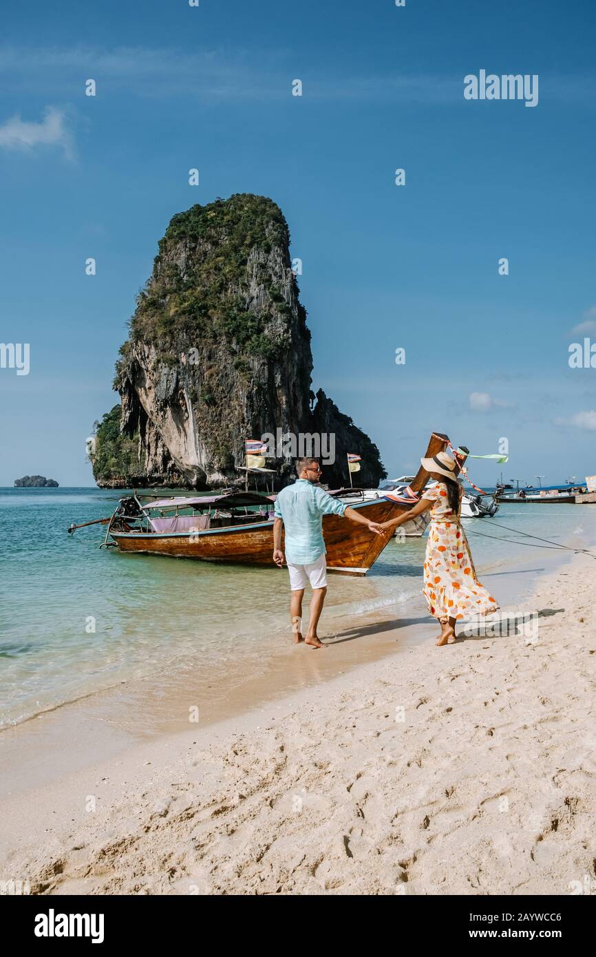 Railay Beach Krabi Thailand, couple walking in the morning on the beach with tropical cliffs and long tail boats on the background at the Island of Stock Photo