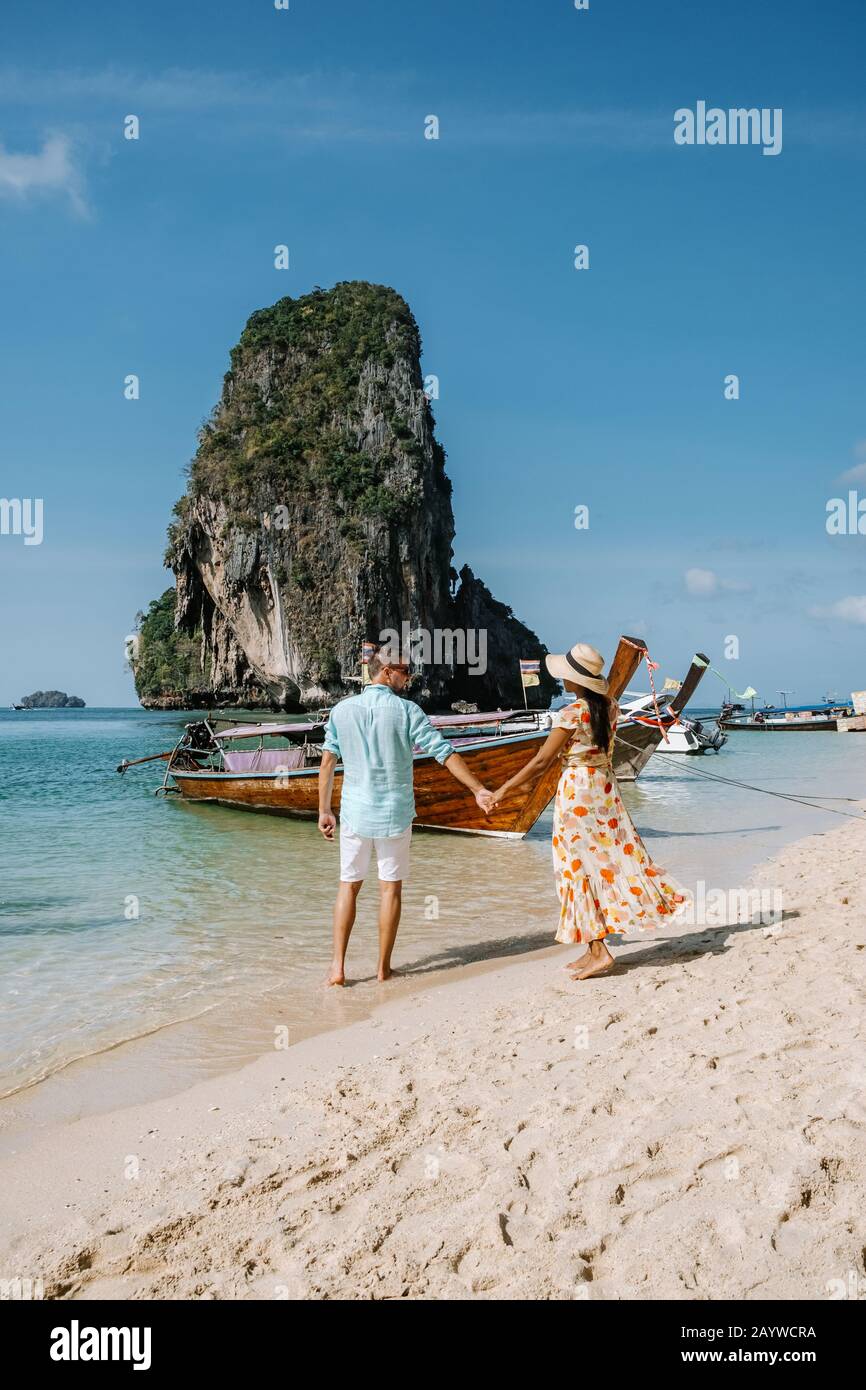 Railay Beach Krabi Thailand, couple walking in the morning on the beach with tropical cliffs and long tail boats on the background at the Island of Stock Photo