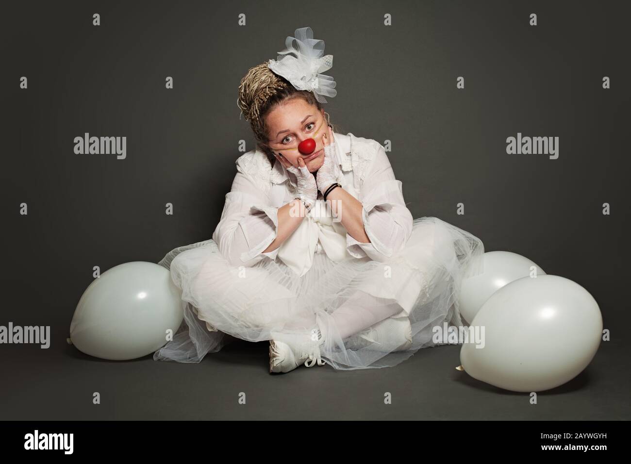 White clown woman sitting on gray background, studio portrait Stock Photo