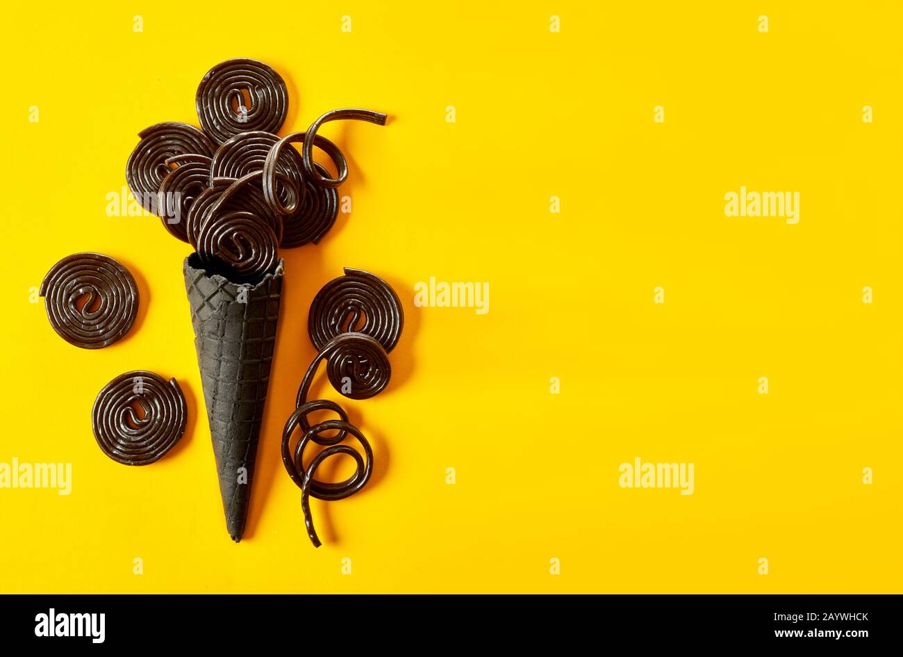 Artistic ice cream in a cone concept with coils of liquorice above a wafer cornet on a brightly colored yellow background with copy space Stock Photo