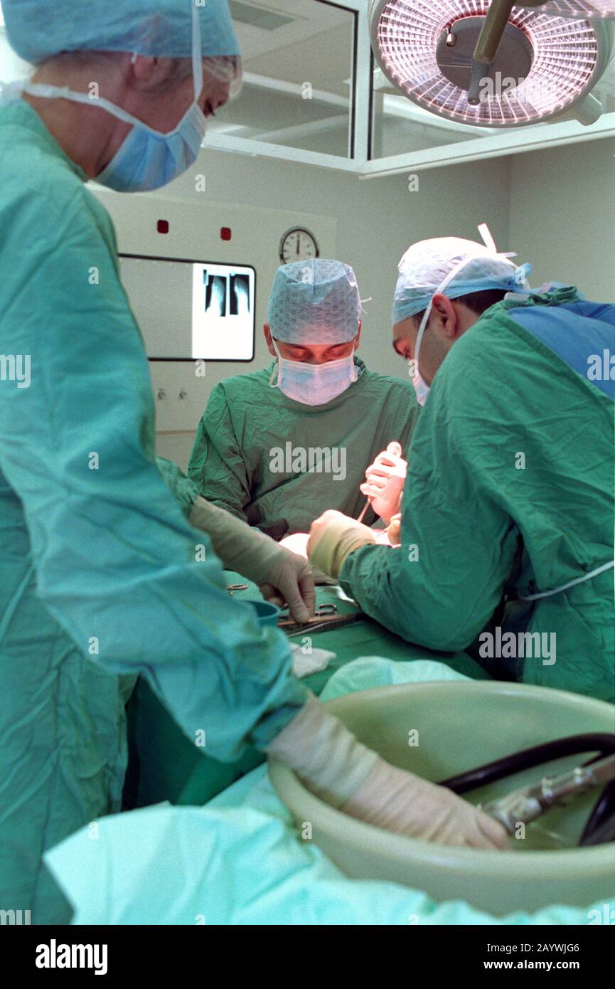 two surgeons in a hospital theatre and the scrub nurse passing surgical instruments Stock Photo