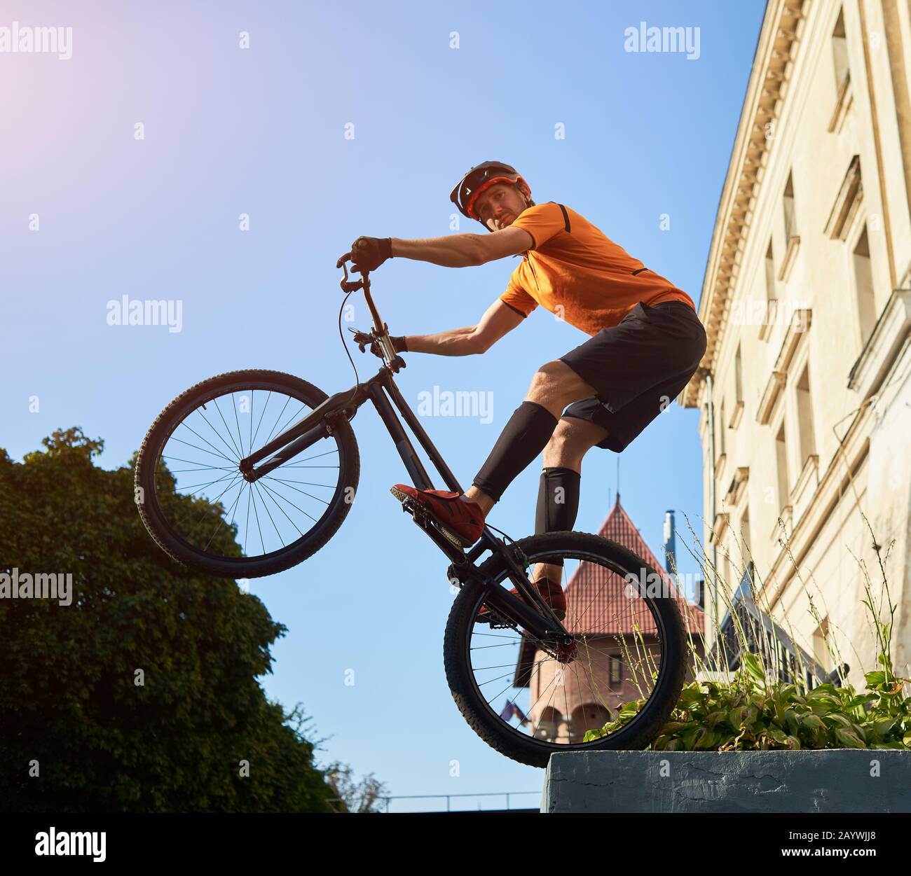 Low angle snapshot of a trial biker standing on a back wheel of mountain bike keeping balance looking at camera, concept of active lifestyle Stock Photo