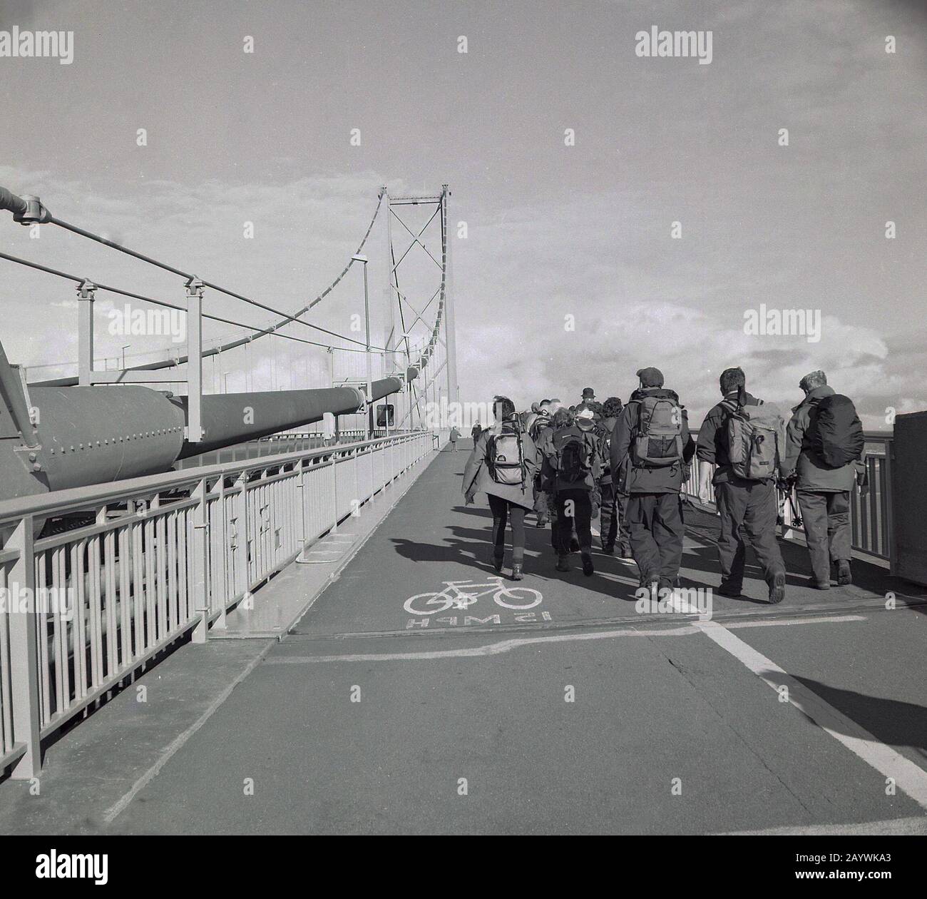 1980s, group of adult walkers in full hiking gear walking along in the pavement and cycle section of the Forth Road Bridge, Stirling, Scotland, one of the world's most significant long span suspension bridges. Stock Photo