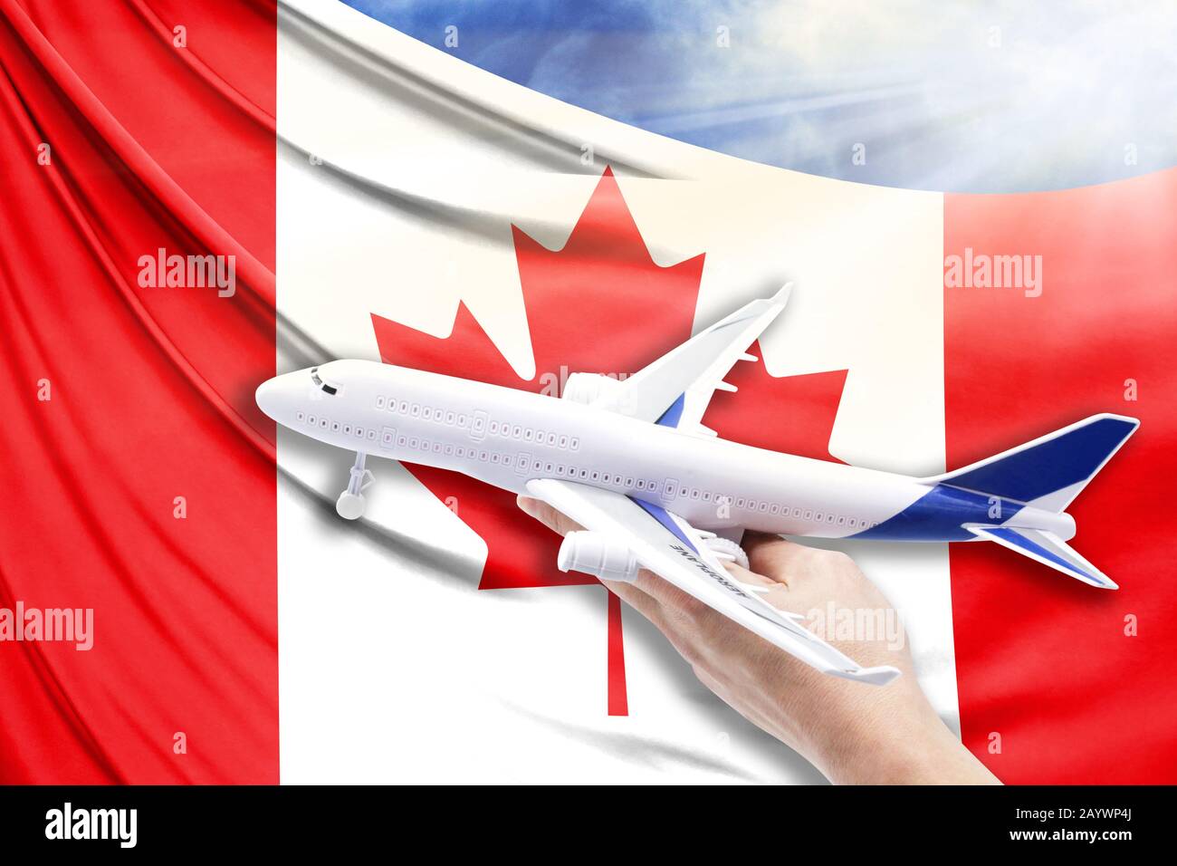 Airplane in hand with national flag of Canada on a background of blue sky with sunbeams Stock Photo