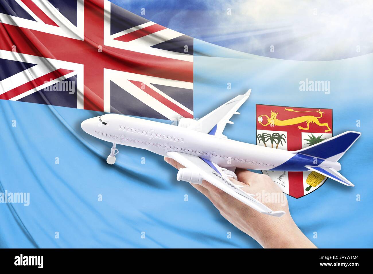 Airplane in hand with national flag of Fiji on a background of blue sky with sunbeams Stock Photo