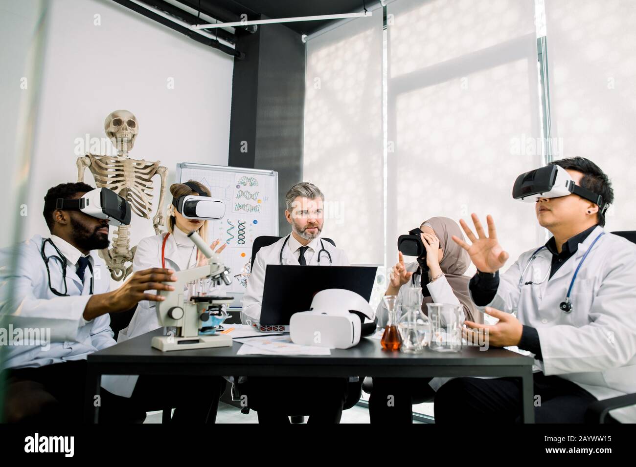 Middle aged male teacher professor has a practical class on microbiology, chemistry with group of multiethnic students, wearing vr goggles while Stock Photo
