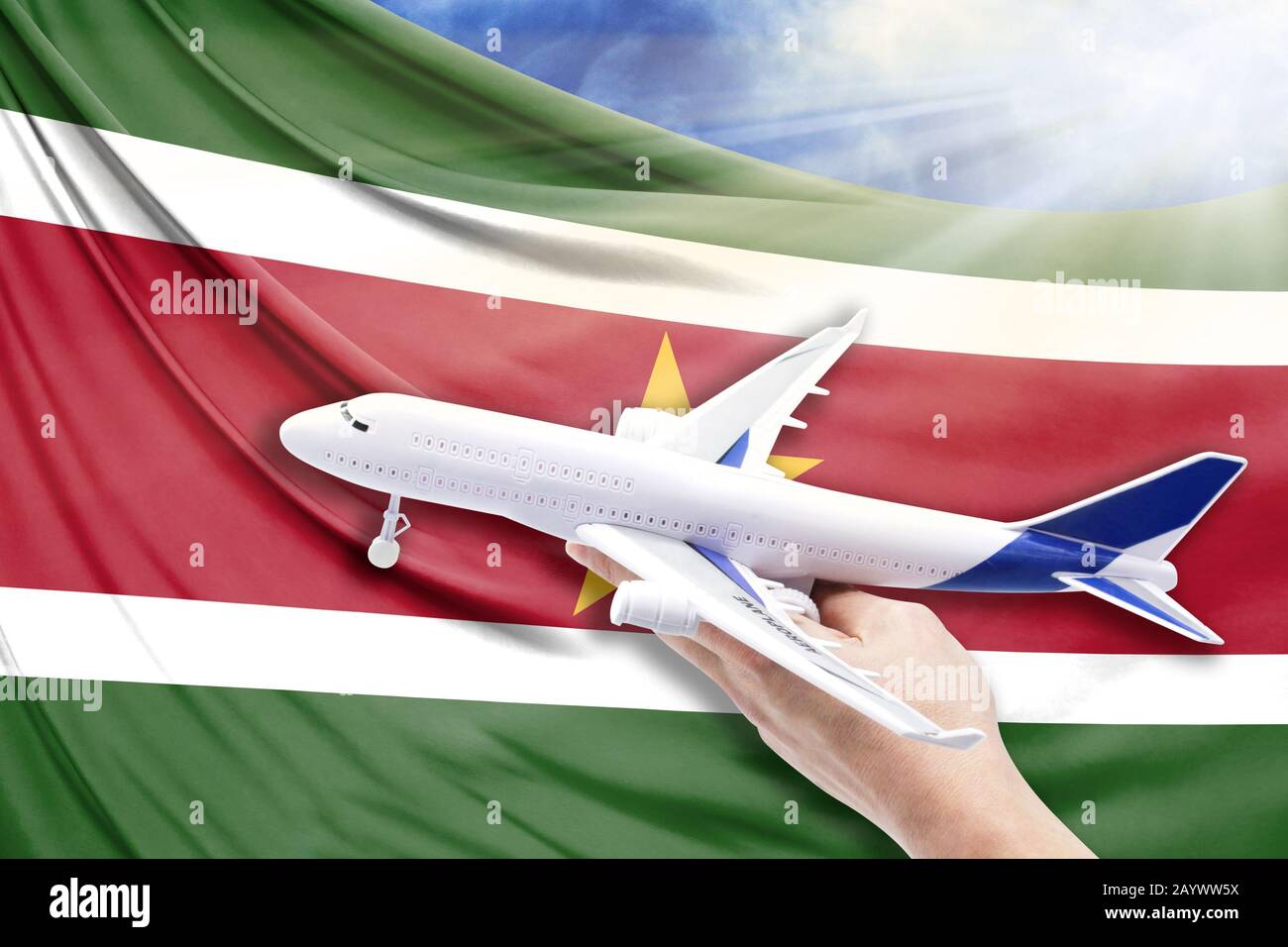 Airplane in hand with national flag of Suriname on a background of blue sky with sunbeams Stock Photo