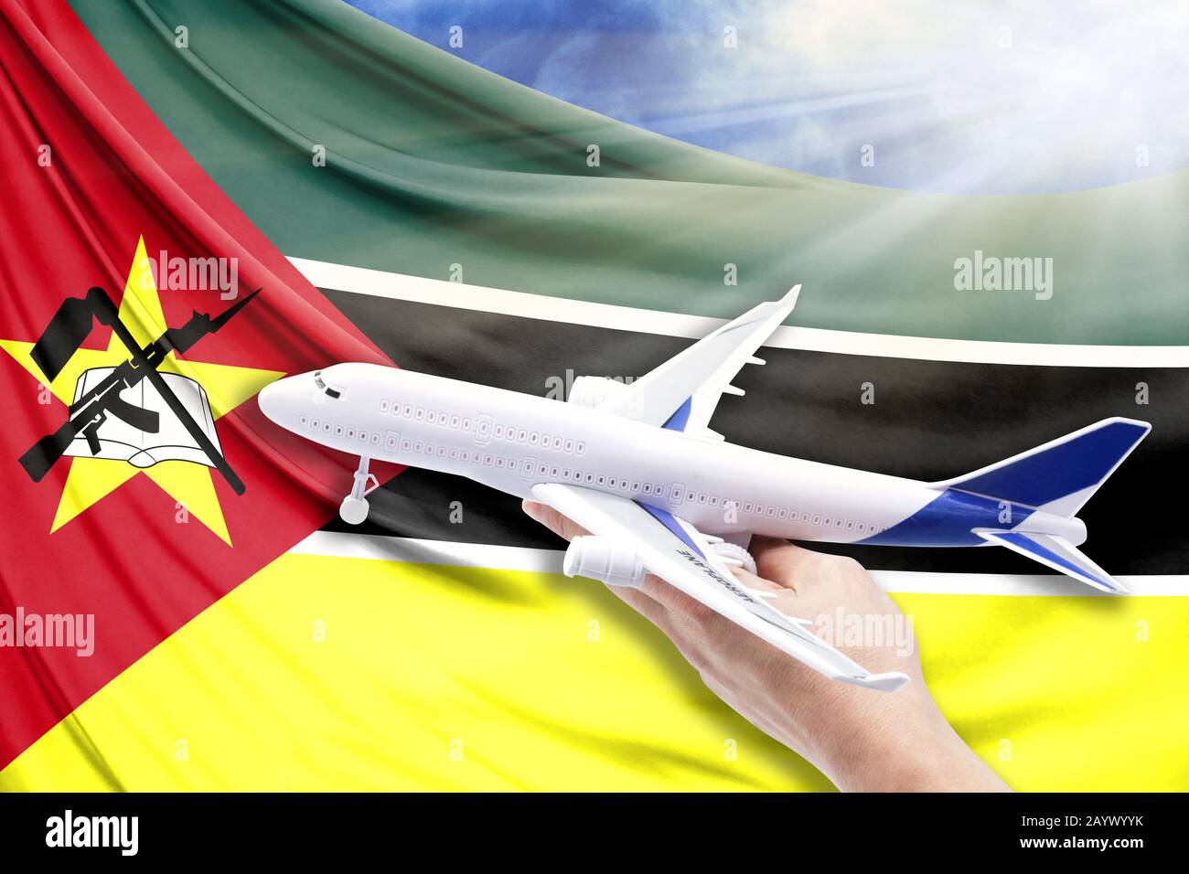 Airplane in hand with national flag of Mozambique on a background of blue sky with sunbeams Stock Photo