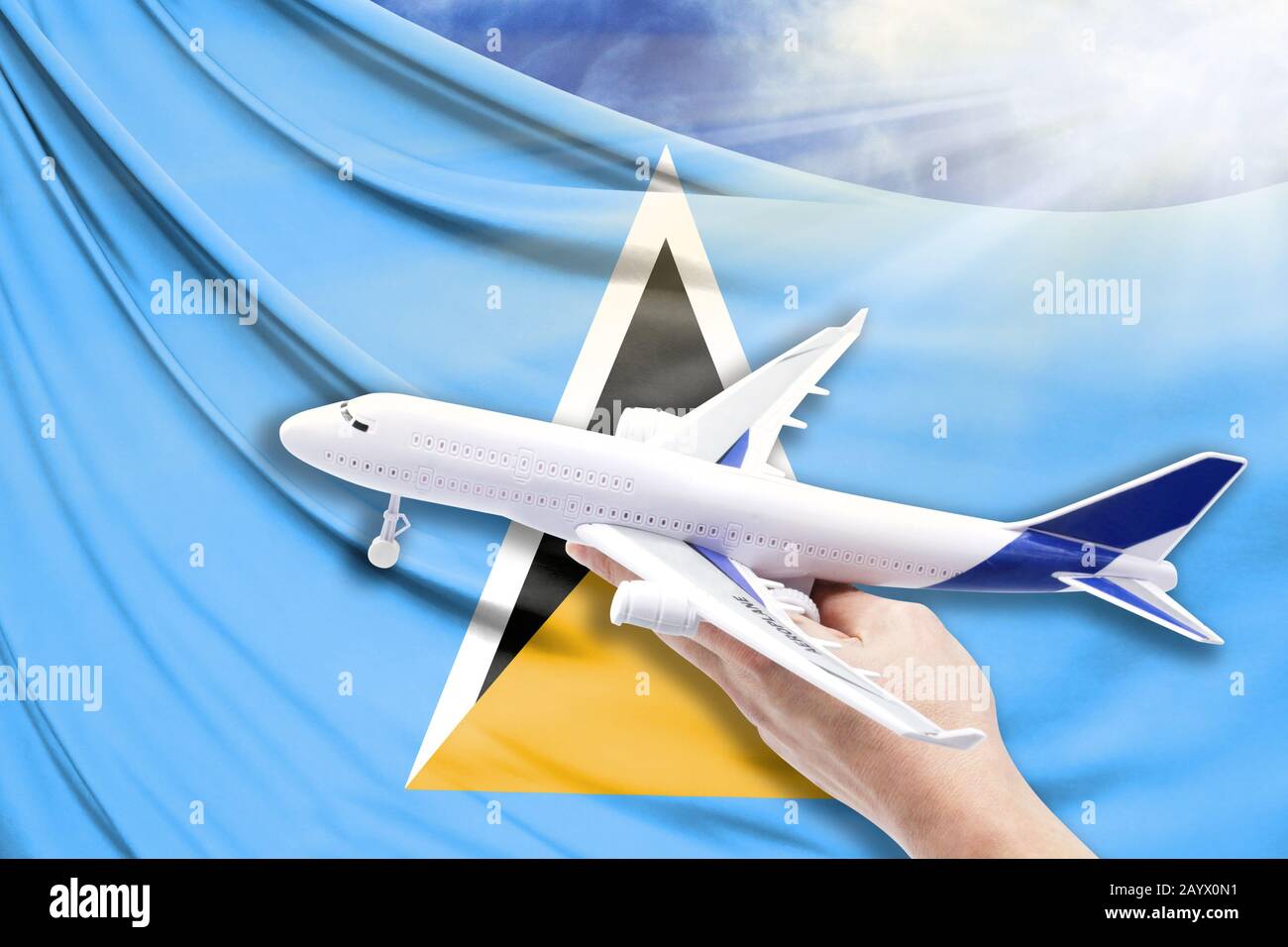 Airplane in hand with national flag of Saint Lucia on a background of blue sky with sunbeams Stock Photo