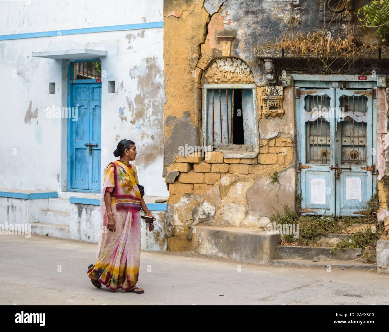 An old Indian woman wearing a colorful saree walks past old dilapidated houses on the streets of the island of Diu. Stock Photo