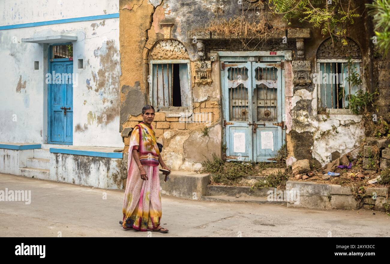 An old Indian woman wearing a colorful saree walks past old dilapidated houses on the streets of the island of Diu. Stock Photo