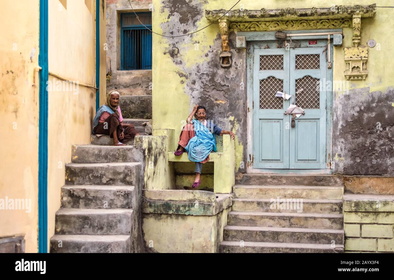 An old Indian woman sits outside the faded doorway of an old house on the streets of the island of Diu . Stock Photo