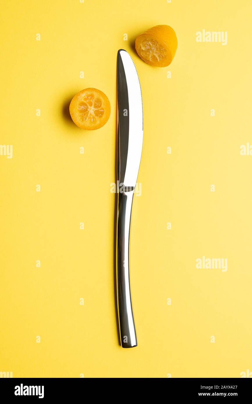 Kumquat fruit opened with knife on yellow background. Stock Photo