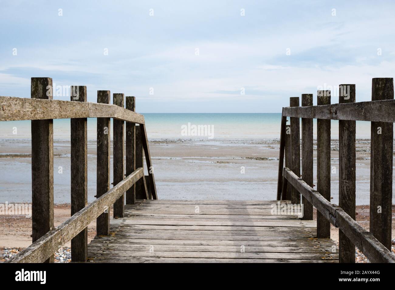 Shot taken from point of view of standing on a wooden bridge, looking out towards the horizon at the beach at low tide. Stock Photo