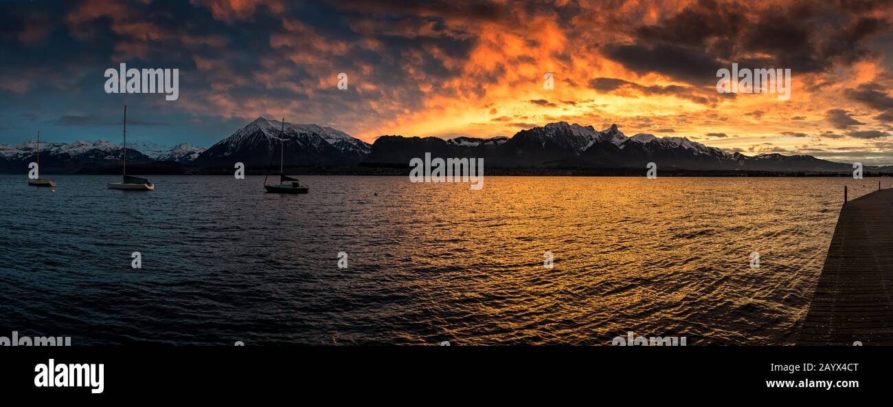 Panorama photo of a red evening sky over Stockhorn mountain range and Niesen reflecting in Lake Thun. Stock Photo