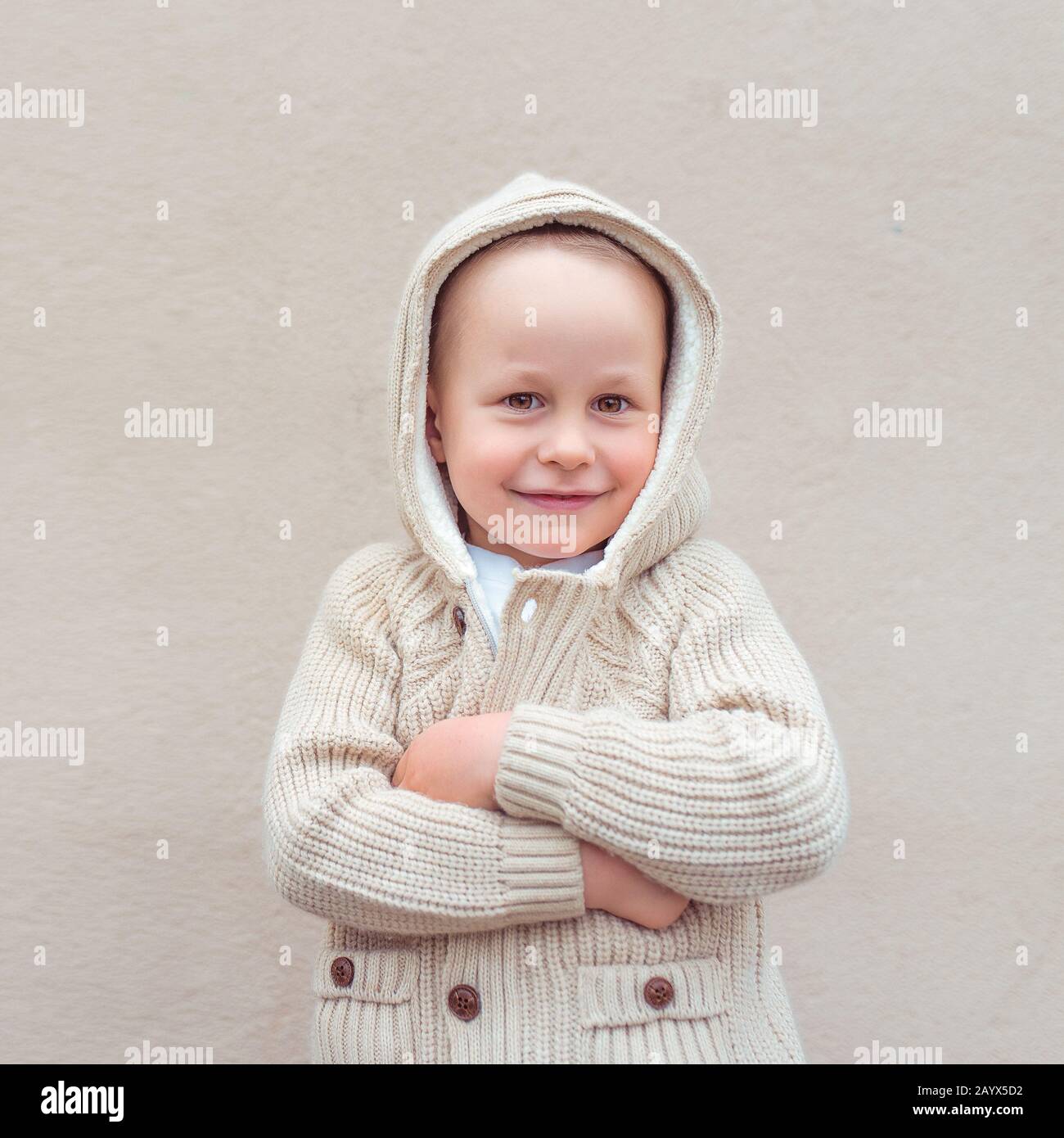 Little boy 4 5 years old stands beige wall in a sweater with a